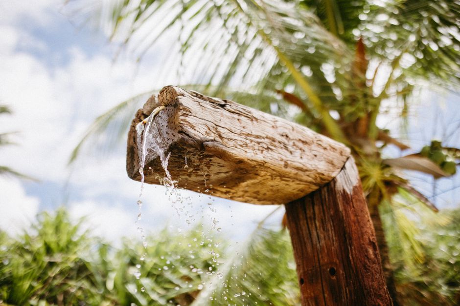 Rustic wooden shower pouring water with tropical palms in background in Maraú, Brazil.
