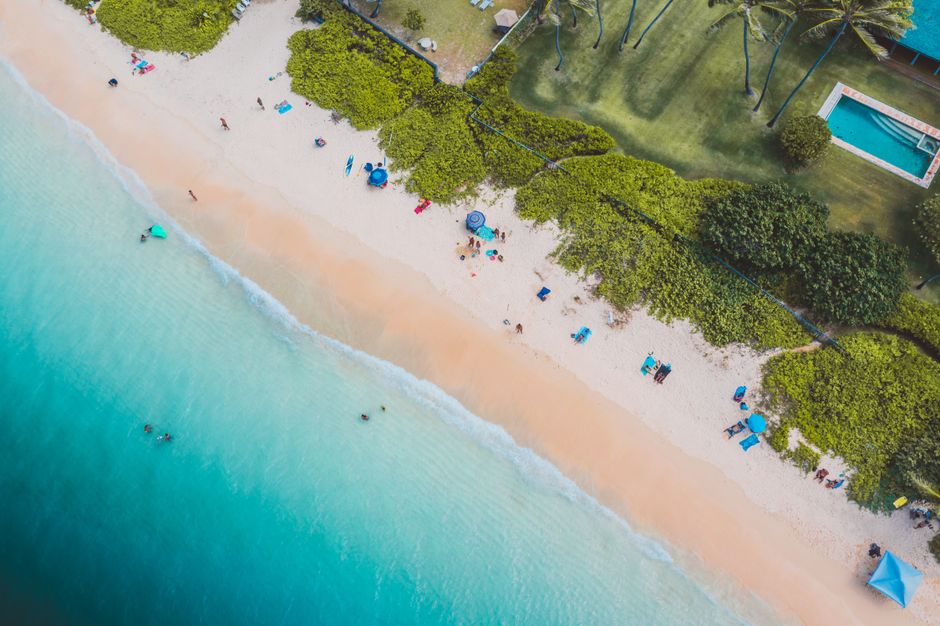 Sunny beach scene with swimmers and umbrellas, captured from above. Ideal for travel and leisure themes.
