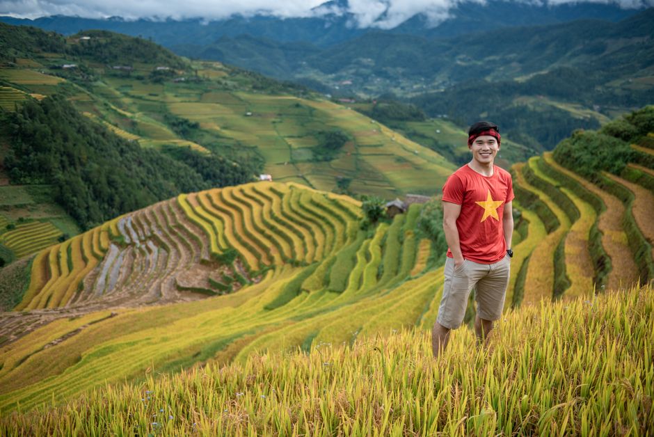 Smiling man in red star t-shirt standing in vibrant terraced rice fields.