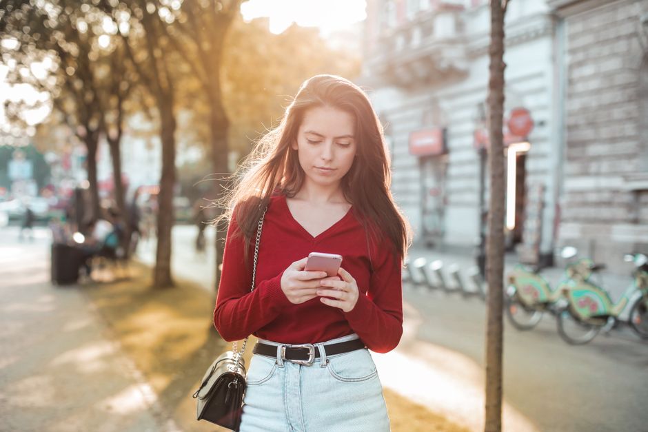 A young woman in casual wear using her smartphone on a sunny day in the city.