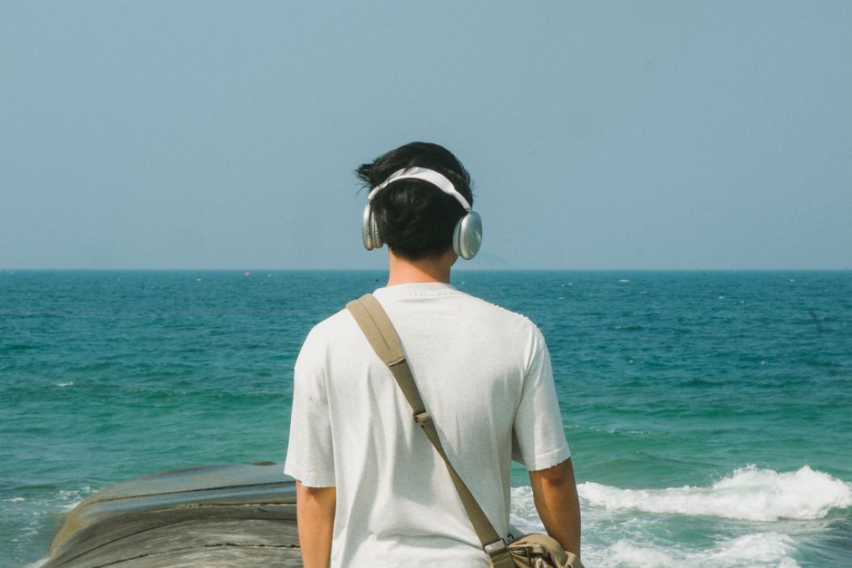 A man wearing headphones stands by the ocean, enjoying a peaceful summer day.