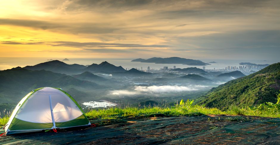 Peaceful campsite with tent overlooking scenic mountains and city at sunset.