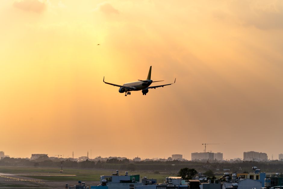 A commercial airplane descends for landing against a vibrant sunset, with city skyline in the background.