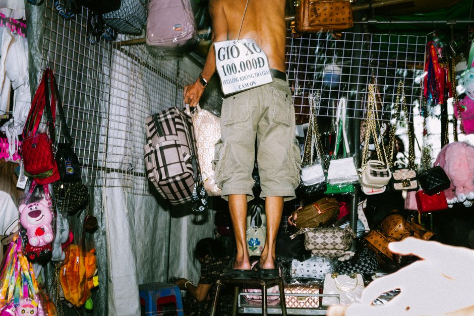 A street vendor selling assorted handbags at a bustling market stall, vibrant and busy.