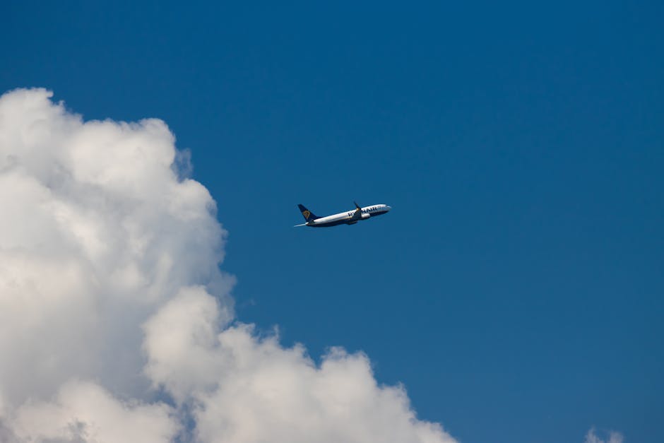A passenger airplane soaring above Corfu, Greece against a bright blue sky and fluffy white clouds.