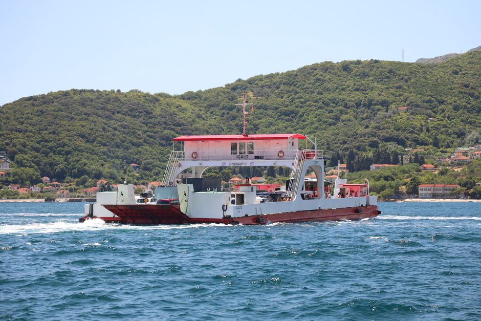 Ferry boat traveling across the Adriatic Sea with lush hills in the background.