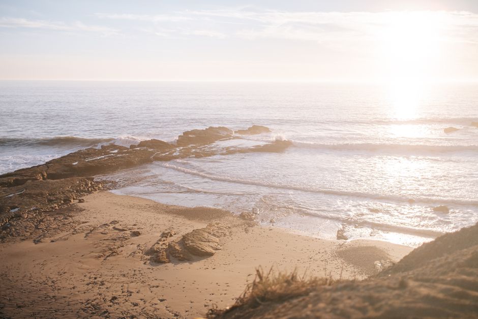 Scenic aerial view of Half Moon Bay's sunny beach with waves crashing on the rocky shore.