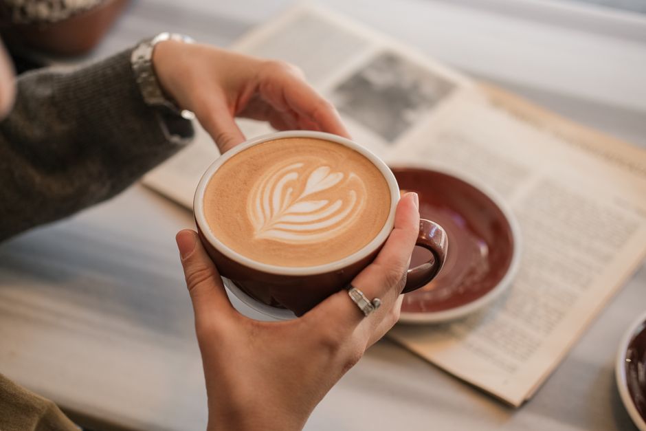Warm coffee latte art with open newspaper in cozy indoor setting.