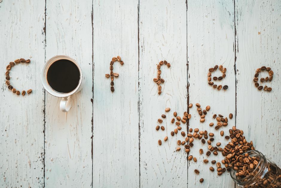 Artistic display of coffee beans spelling 'coffee' with a cup on a rustic wooden table.