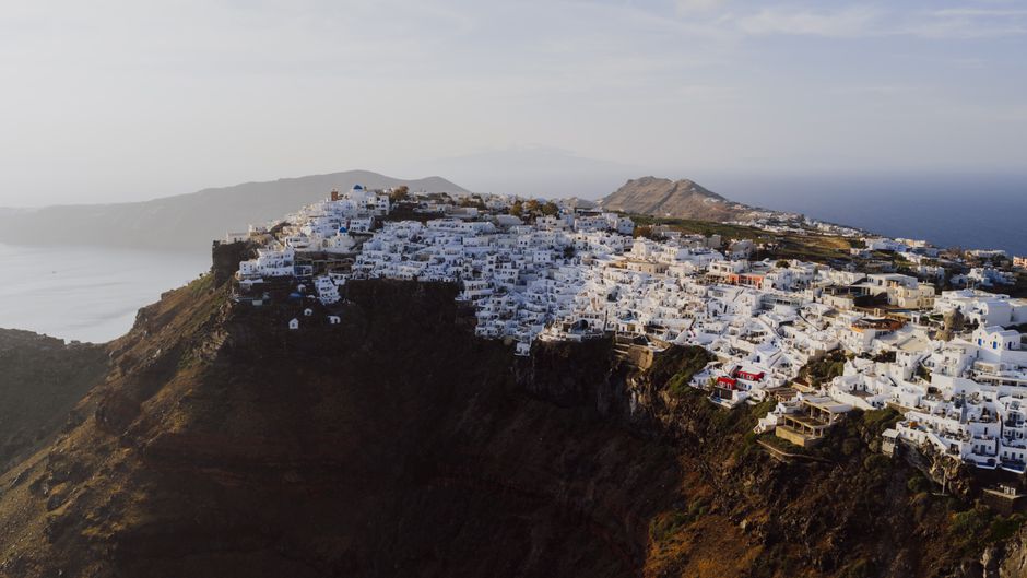 Breathtaking aerial view of Fira's iconic white buildings perched on cliffs with a view of the Aegean Sea in Greece.