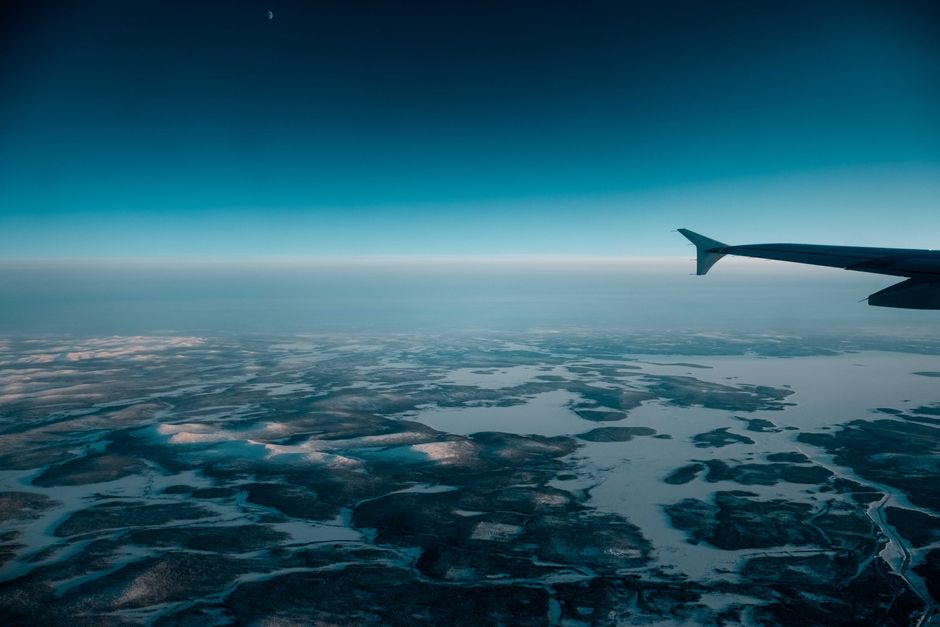Tail of aircraft flying in cloudless evening sky over wetland covered with snow