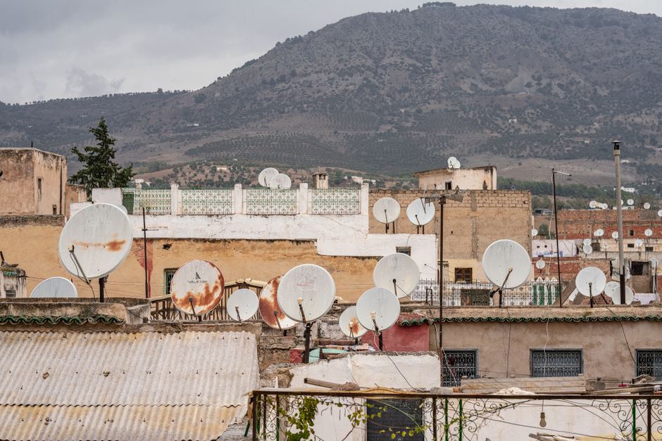 Rustic rooftops with satellite dishes in Fes, set against a rolling hill landscape.