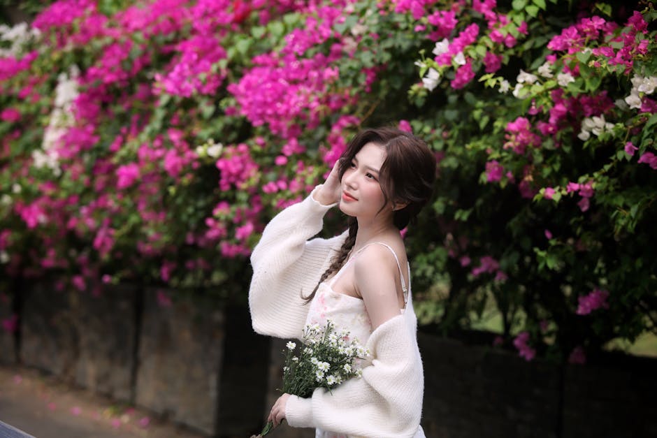Smiling woman with flowers in white dress by vibrant Bougainvillea hedge.