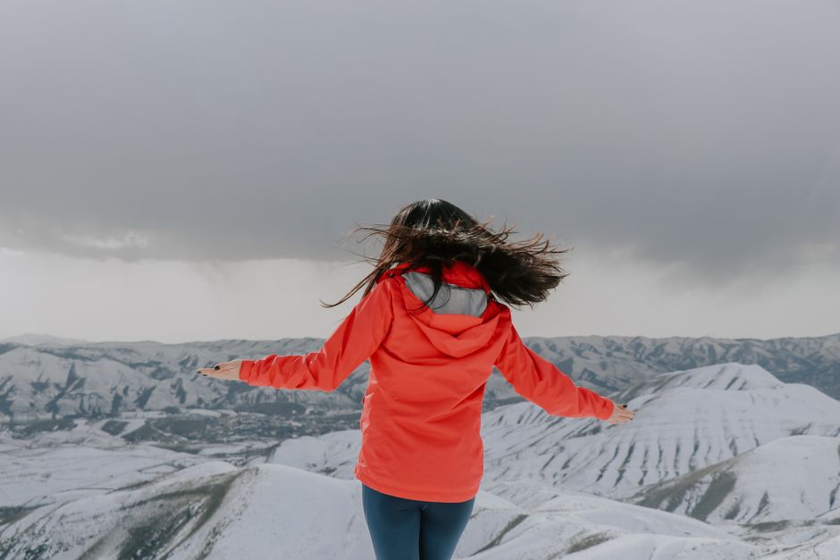 Woman in red jacket embracing snowy mountain panorama with arms open wide.