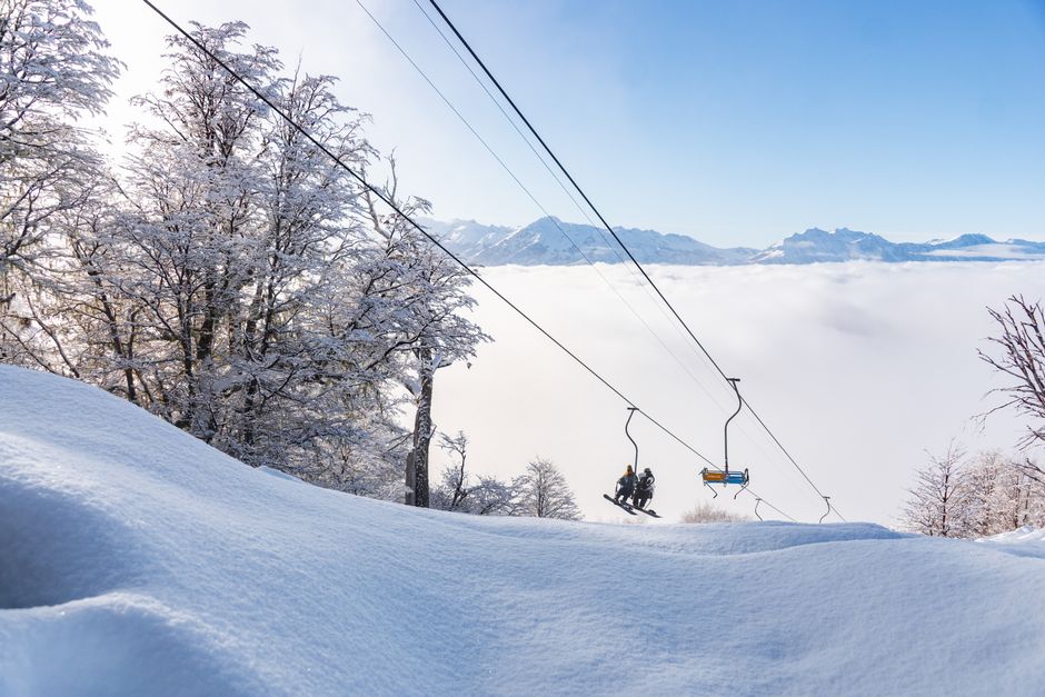 Winter landscape with skiers on a chairlift above snow-covered mountains in El Bolsón, Argentina.