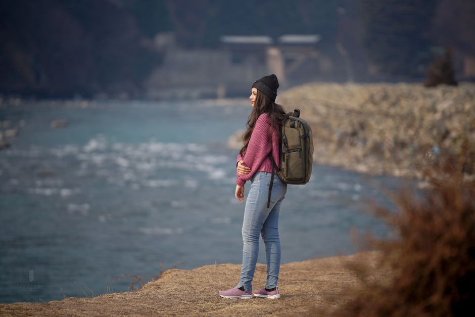Young woman in pink sweater with backpack enjoying peaceful riverside view. Ideal for travel and leisure themes.