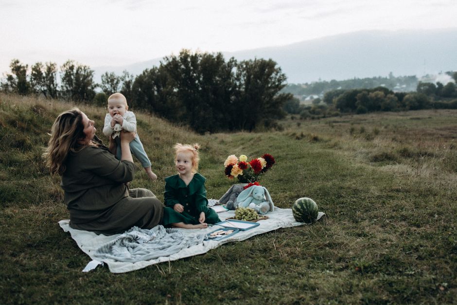 Mother with children having a joyful picnic outdoors on a blanket with scenic landscape views.