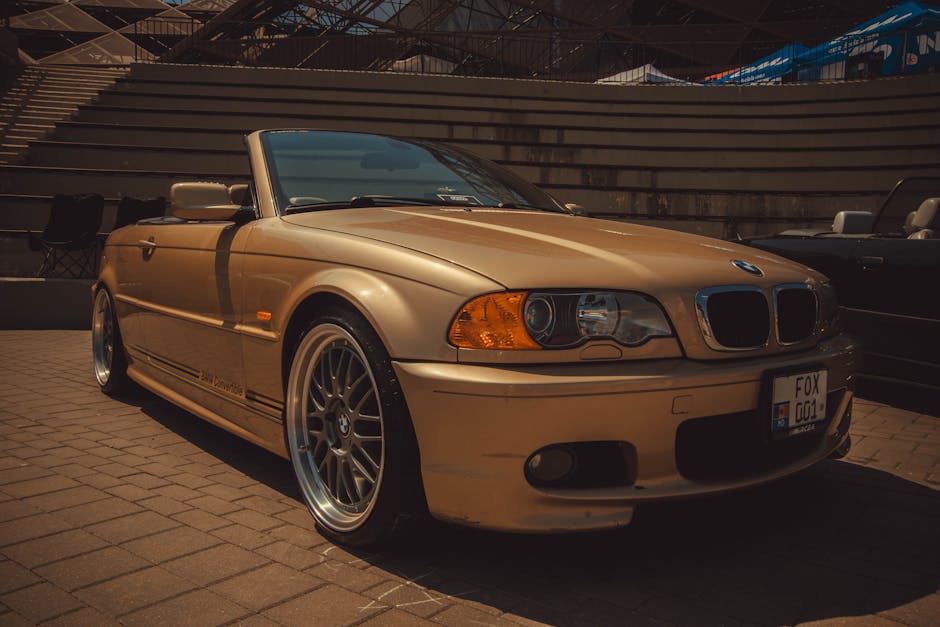 A luxurious gold convertible car parked outdoors in a sunlit urban location.