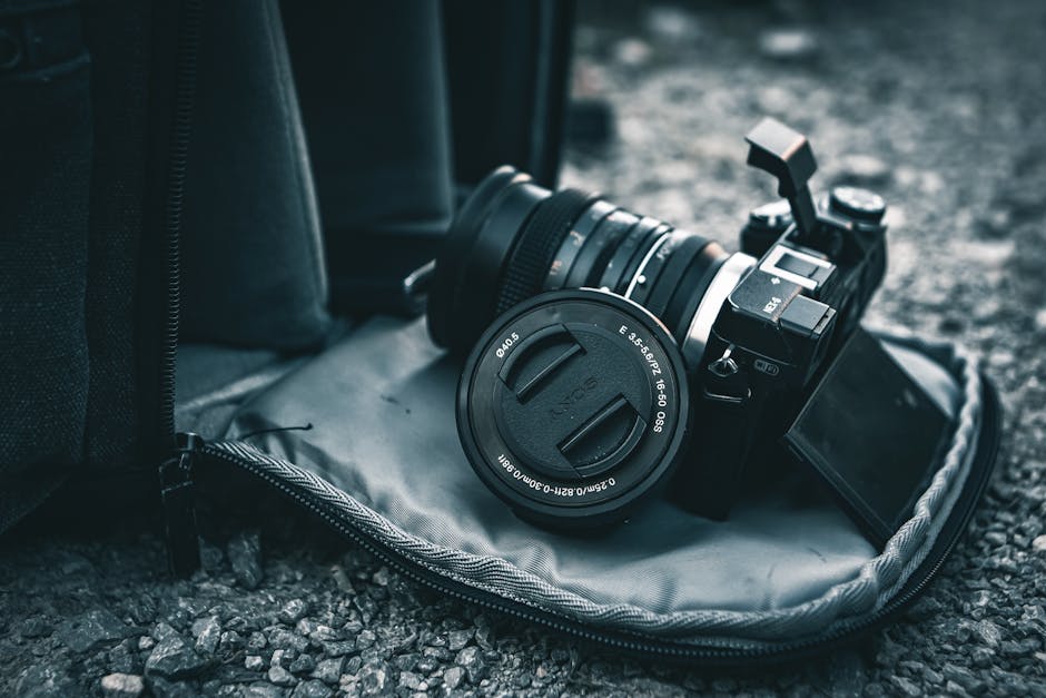 Close-up of a mirrorless camera resting on a gray bag on gravel.