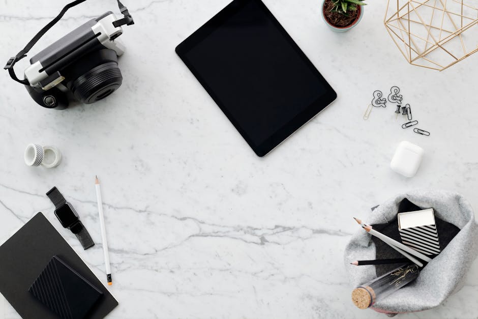 Flat lay of a modern workspace featuring a tablet, camera, and office supplies on a marble surface.