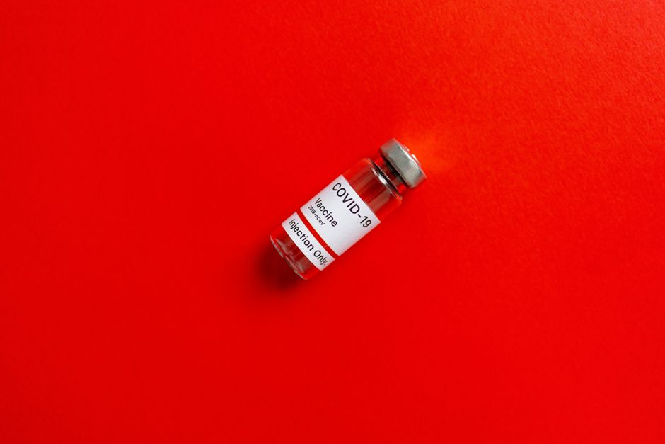 Close-up of a COVID-19 vaccine vial against a vivid red surface, symbolizing health and vaccination.