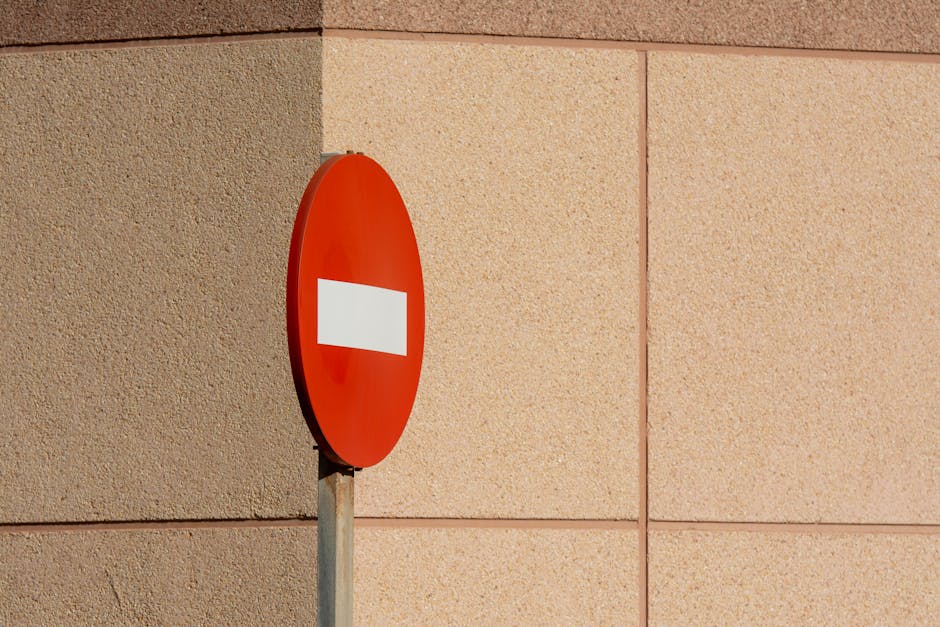 Urban image of a no-entry road sign against a beige tiled exterior wall.
