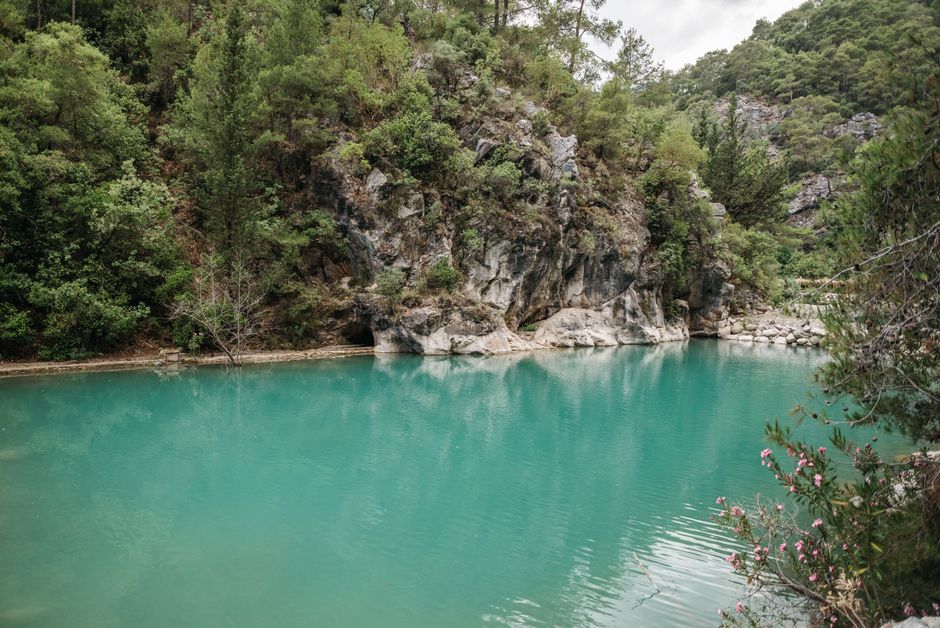 Tranquil turquoise lake surrounded by lush greenery and rocky cliffs in a serene natural setting.